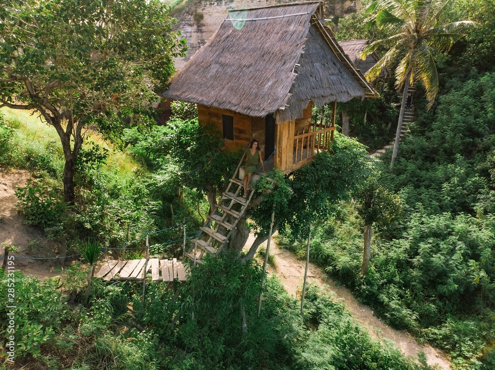 Traditional house on tree, woman siton stairs and  look at Atun beach, Nusa Penida island. Popular travel destination on Bali holidays. Indonesia