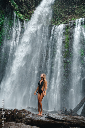 Woman enjoying near hidden in jungle huge waterfall in Indonesia. Slim body and black swimsuit  fashion model. Travelling  Indonesia