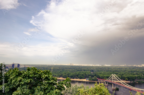 View of pedestrian Park bridge over the Dnipro river. Cloudy sky after rain. Summertime photo