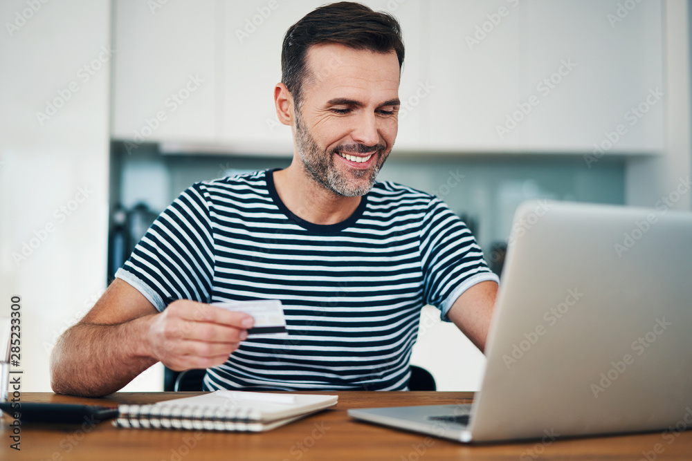 Happy man sitting at home paying bills online with credit card and laptop Happy man sitting at home paying bills online with credit card and laptop