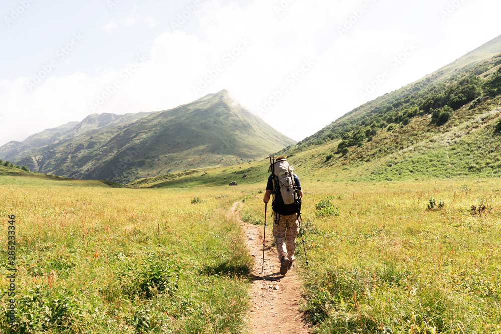 A man with a heavy backpack goes along the path to an expedition in the mountains.