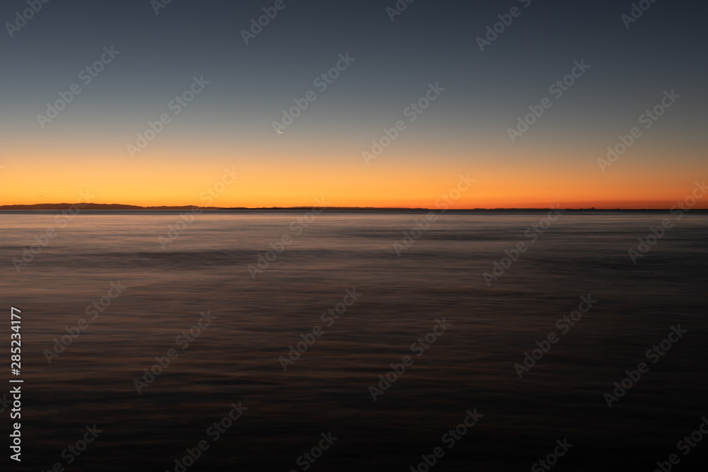 A long exposure captures the crescent moon overlooking over the beautiful gradient created by the sun after it has set into the horizon on North Stradbroke Island, Queensland, Australia