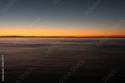 A long exposure captures the crescent moon overlooking over the beautiful gradient created by the sun after it has set into the horizon on North Stradbroke Island, Queensland, Australia © Hal Photography