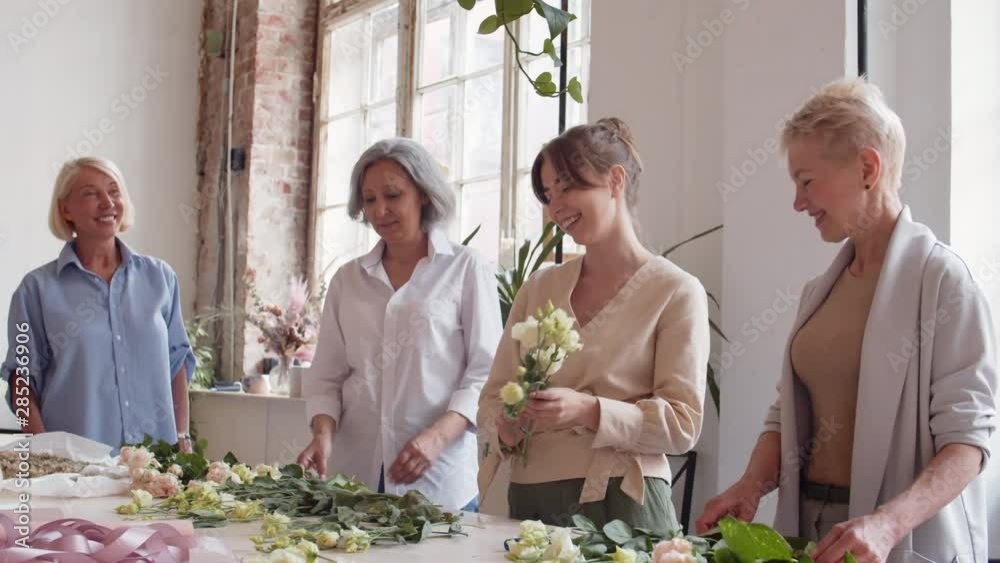 Panning of four Caucasian women standing at table in workshop and discussing flowers