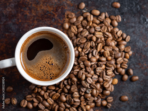 A Cup of espresso on a rusty background with scattered roasted coffee beans . copy space