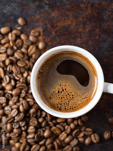 A Cup of espresso on a rusty background with scattered roasted coffee beans