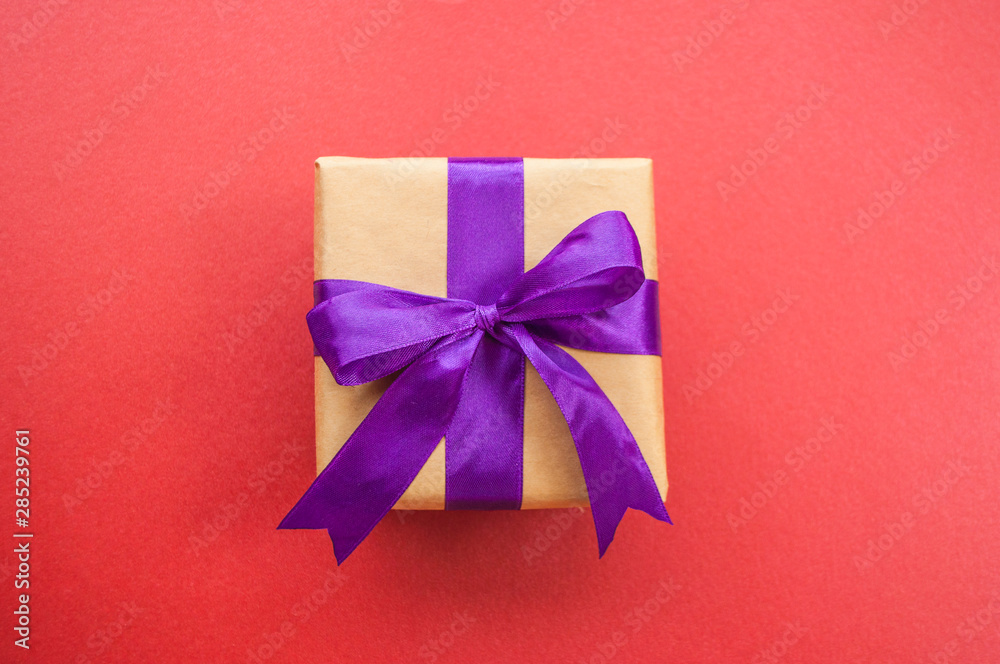Giftbox tied with purple color ribbon on dark red background. Flat lay style.