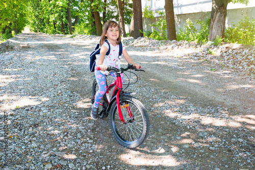 A little girl with a backpack riding a bike in the park on a rocky road.