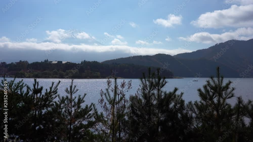 Static shot of a lake and trees with Fuji mountain in the background covered by low clouds in Japan Static shot of a lake and trees with Fuji mountain in the background covered by low clouds in Japan