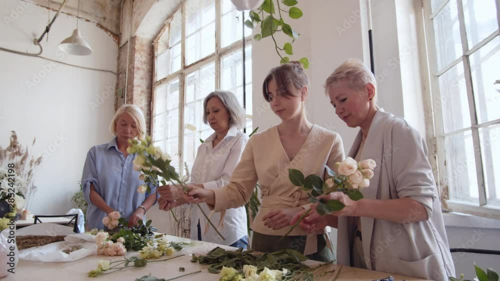 Four Caucasian women standing at table in workshop and looking through flowers Four Caucasian women standing at table in workshop and looking through flowers