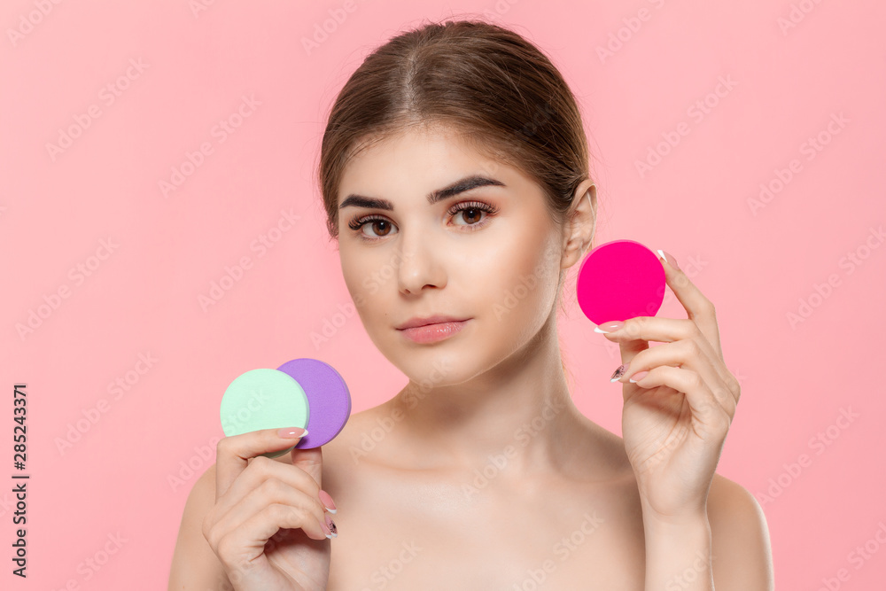 Beautiful model holds cotton sponges of different colors close to face.