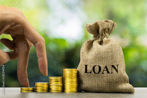 Financial loan agreement concept. A man hand on growth stack of coins and loan bag on wooden table. photo
