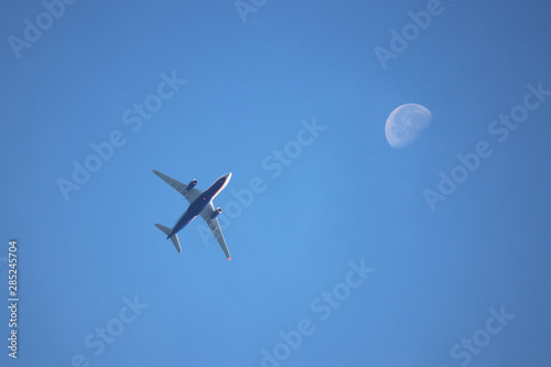 Airplane flying in the blue sky on background of waning moon in the morning. Commercial twin-engine plane taking off, air travel concept