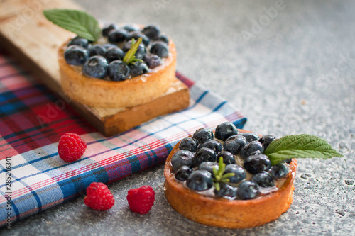 Tartlets with blueberries on the gray table with a checkered napkin, with fresh berries of raspberry. Top view