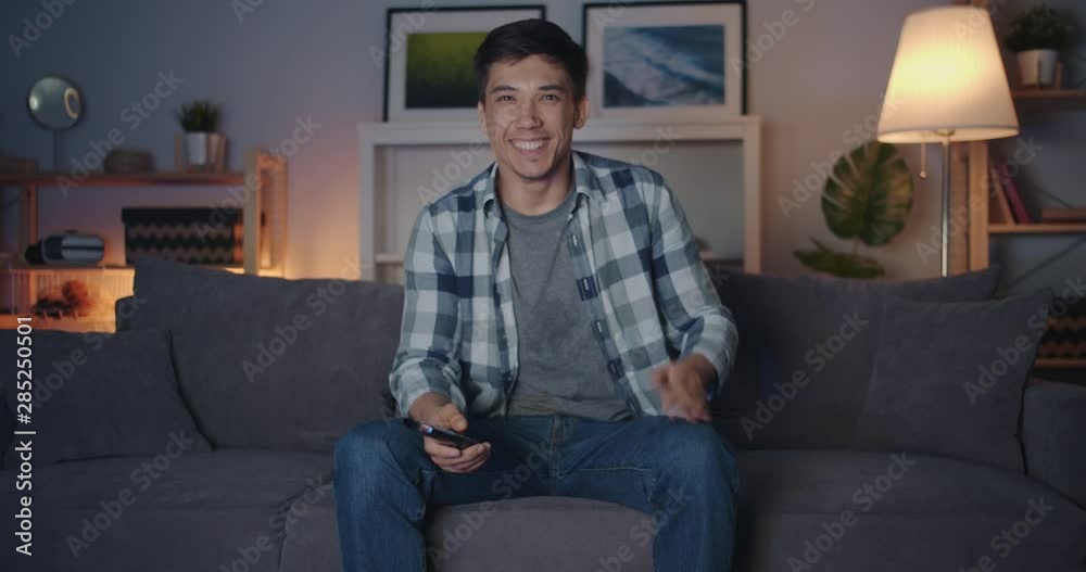 Portrait of mixed race young man watching TV at night laughing having fun sitting on couch at home and looking at camera. Happiness and people concept. Portrait of mixed race young man watching TV at night laughing having fun sitting on couch at home and looking at camera. Happiness and people concept.