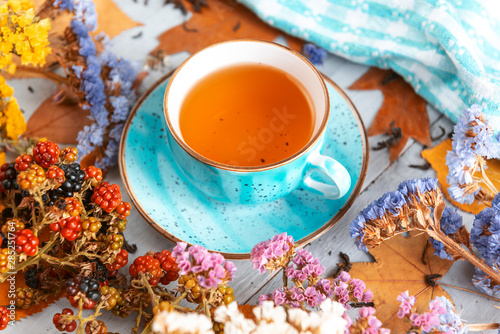 composition still life of a mug with hot leaf tea with berries and autumn leaves on a wooden surface