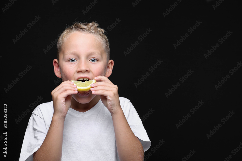 Little, blond boy is eating a piece of a lemon in front of black background with blue eyes. Little, blond boy is eating a piece of a lemon in front of black background with blue eyes.