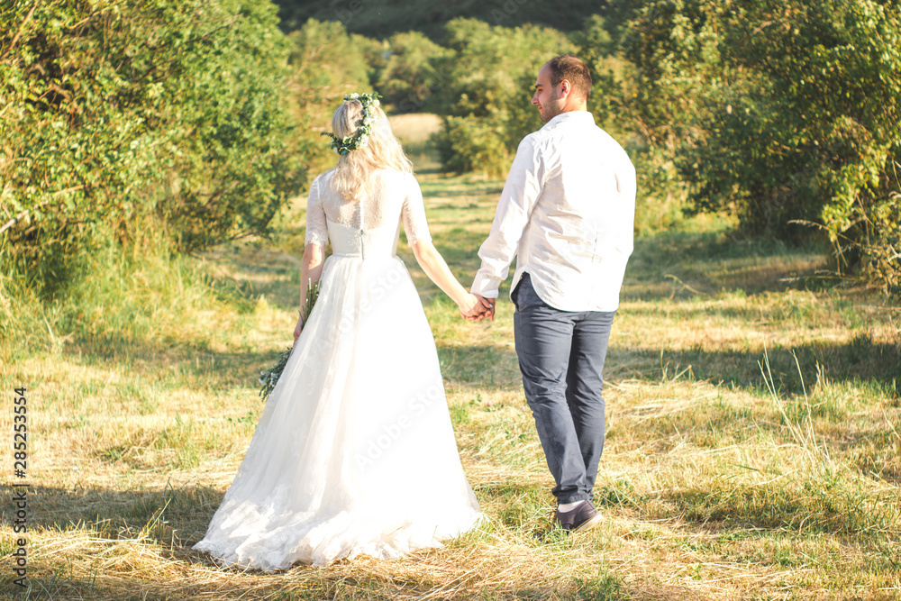 Back view on bride and groom holding hands in sunny summer day. Outdoor wedding and relationsheep romantic concept
