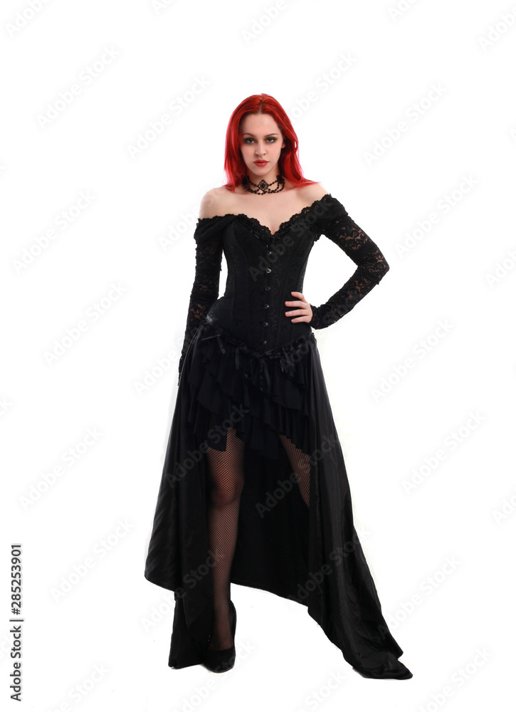 full length portrait of a  red haired girl wearing a  black gothic gown, Standing pose on a grey studio background.