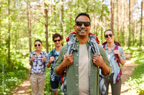 travel, tourism, hike and people concept - indian man in sunglasses and group of friends with backpacks in forest