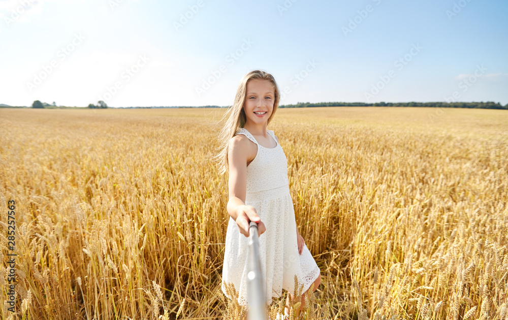 technology, summer and people concept - happy young girl in white dress taking picture by selfie stick on cereal field technology, summer and people concept - happy young girl in white dress taking picture by selfie stick on cereal field