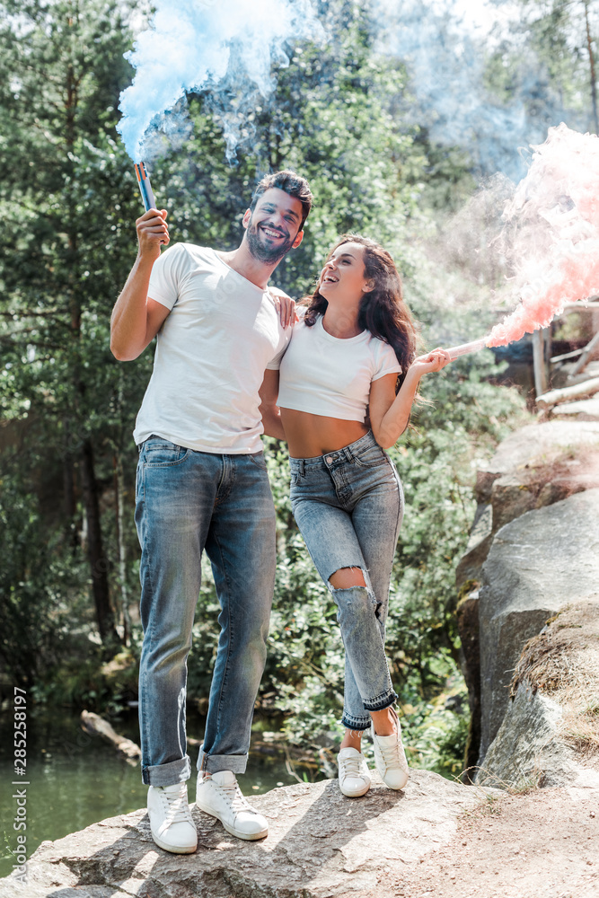 happy bearded man and attractive woman holding smoke bombs