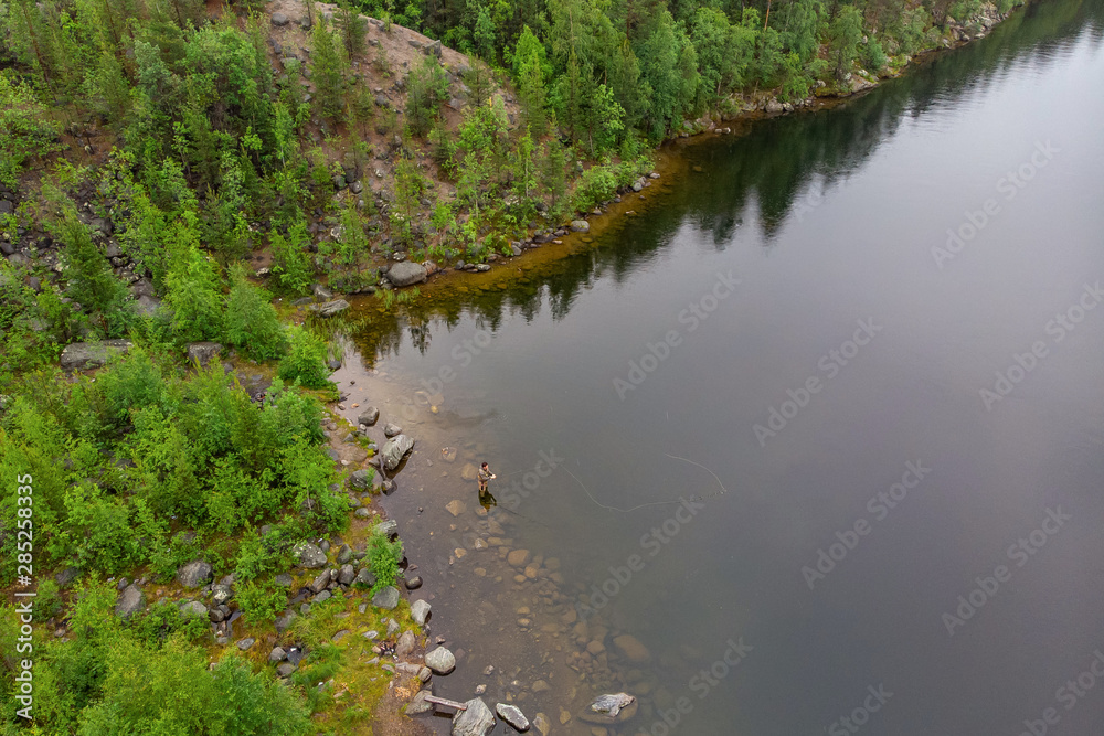 Fisherman man casts rod in mountain river in boots fly fishing salmon, morning. Aerial top view Fisherman man casts rod in mountain river in boots fly fishing salmon, morning. Aerial top view