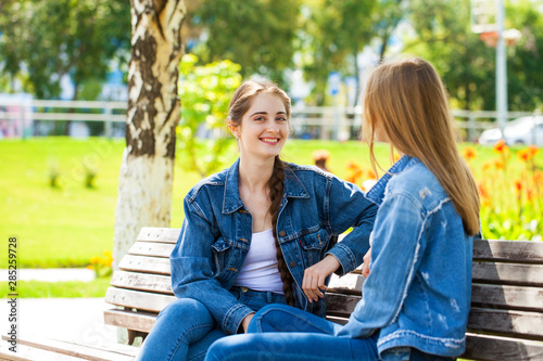 Two beautiful girlfriends are talking in a park sitting on a bench