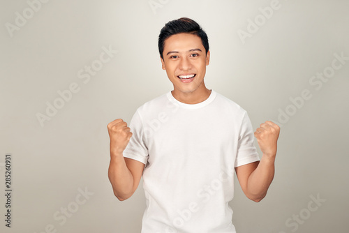 Successful emotional young asian male raising clenched fists in the air, feeling excited.