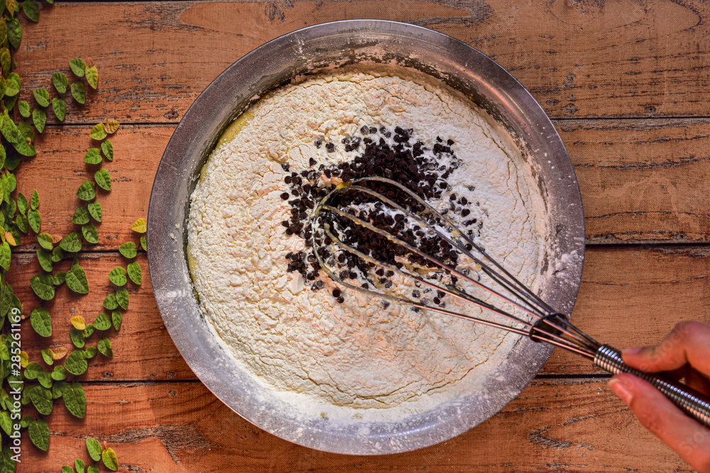 Bowl with ingredients to make a cake with chocolate chips on a wooden surface Bowl with ingredients to make a cake with chocolate chips on a wooden surface