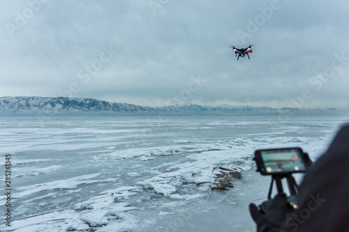 Man flies black drone helicopter over frozen lake