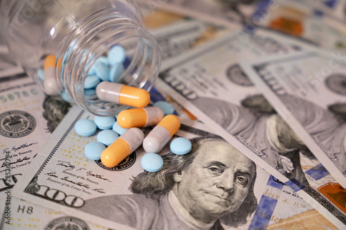 Pills and capsules in a bottle on US dollars bills. Concept of health care, pharmaceutical business, drug prices, pharmacy, medicine and economics