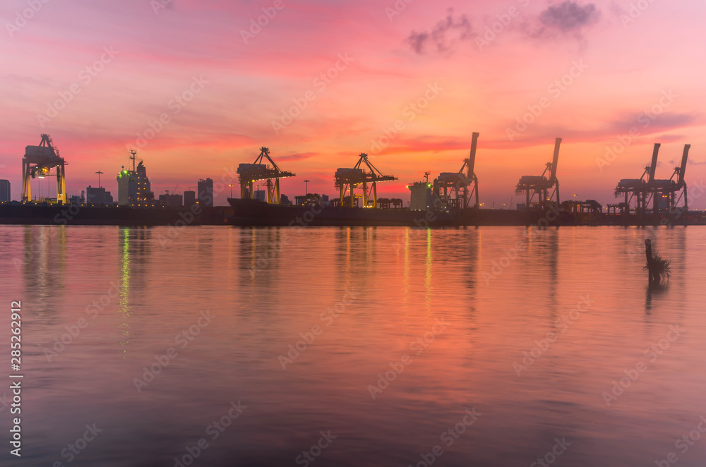 Silhouette container cargo freight ship with working crane bridge in shipyard with sunrise twilight colorful sky for Logistic Import Export background