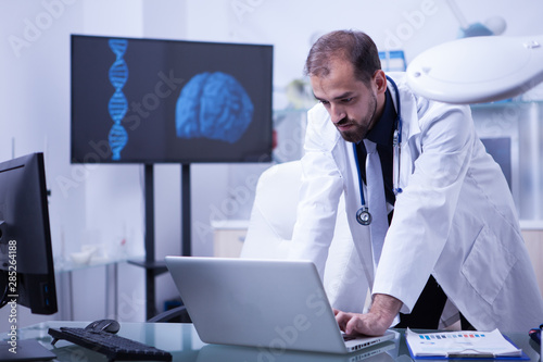 Doctor working on laptop with brain image in the background