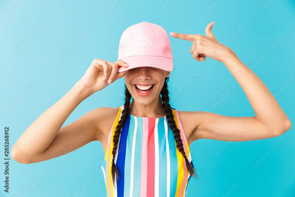 Image of cheerful brunette girl wearing summer dress and cap smiling at camera Image of cheerful brunette girl wearing summer dress and cap smiling at camera