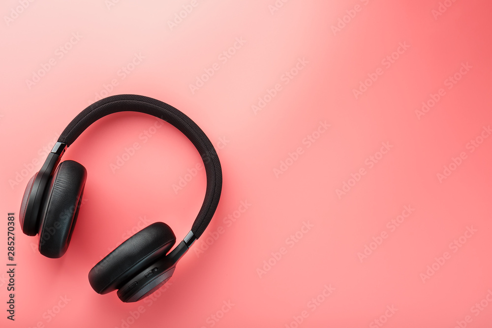 Wireless black headphones on a pink background. View from above. In-ear headphones for playing games and listening to music tracks. Wireless black headphones on a pink background. View from above. In-ear headphones for playing games and listening to music tracks.