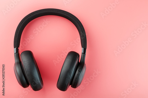 Wireless black headphones on a pink background. View from above. In-ear headphones for playing games and listening to music tracks.