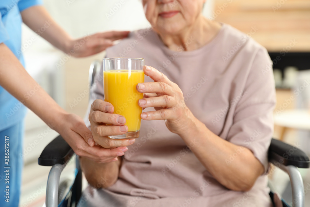 Nurse giving glass of juice to elderly woman indoors, closeup. Assisting senior people Nurse giving glass of juice to elderly woman indoors, closeup. Assisting senior people