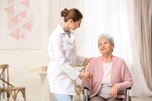 Nurse assisting elderly woman in wheelchair indoors photo