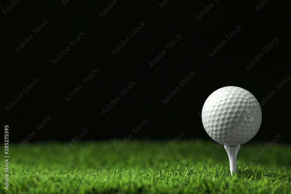 Golf ball with tee on artificial grass against black background, space for text Golf ball with tee on artificial grass against black background, space for text
