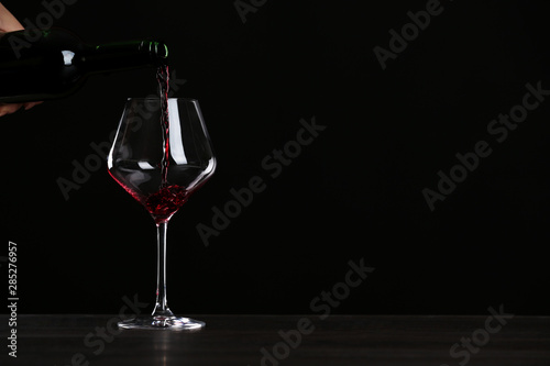 Woman pouring wine into glass on table against black background, closeup with space for text