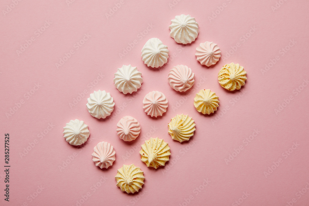 Top view of white, pink and yellow meringues in rows on pink background Top view of white, pink and yellow meringues in rows on pink background