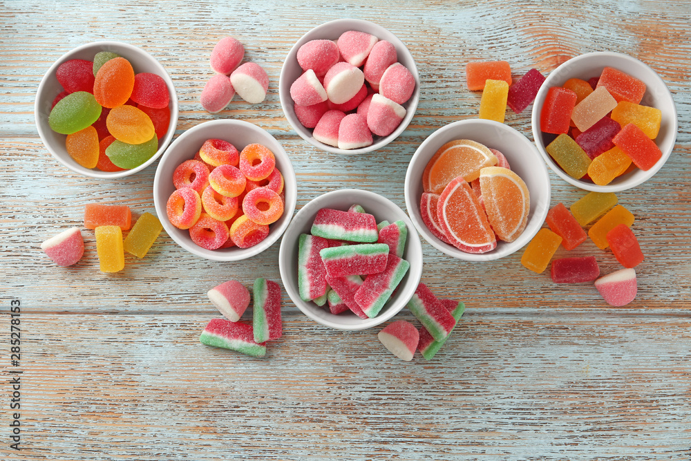 Flat lay composition with bowls of different jelly candies on wooden background