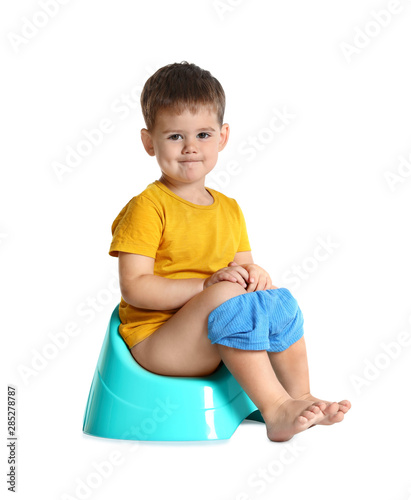 Portrait of little boy sitting on potty against white background photo