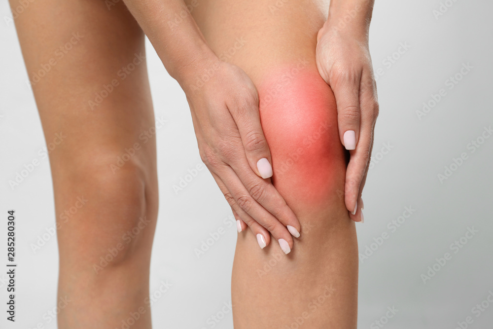 Woman having knee problems on grey background, closeup