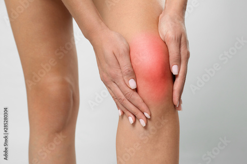 Woman having knee problems on grey background  closeup