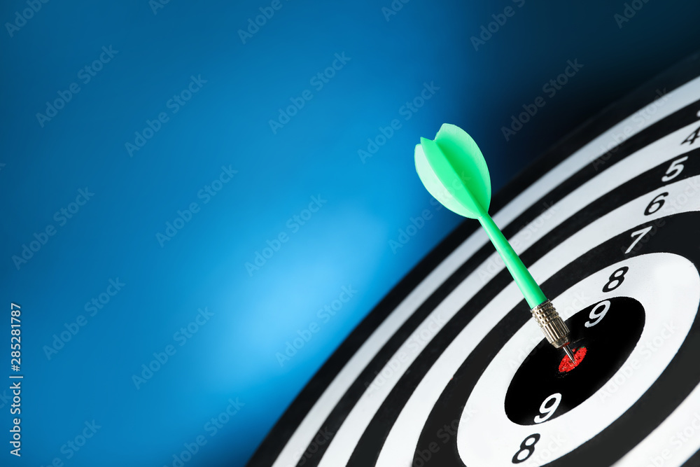 Green arrow hitting target on dart board against blue background. Space for text Green arrow hitting target on dart board against blue background. Space for text