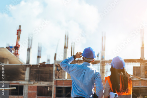 Asian man civil engineer and woman architect wearing blue safety helmet meeting at contruction site.