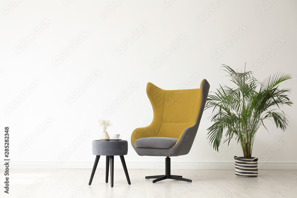 Fototapeta premium Stylish living room interior with comfortable armchair and houseplant near white wall. Space for text
