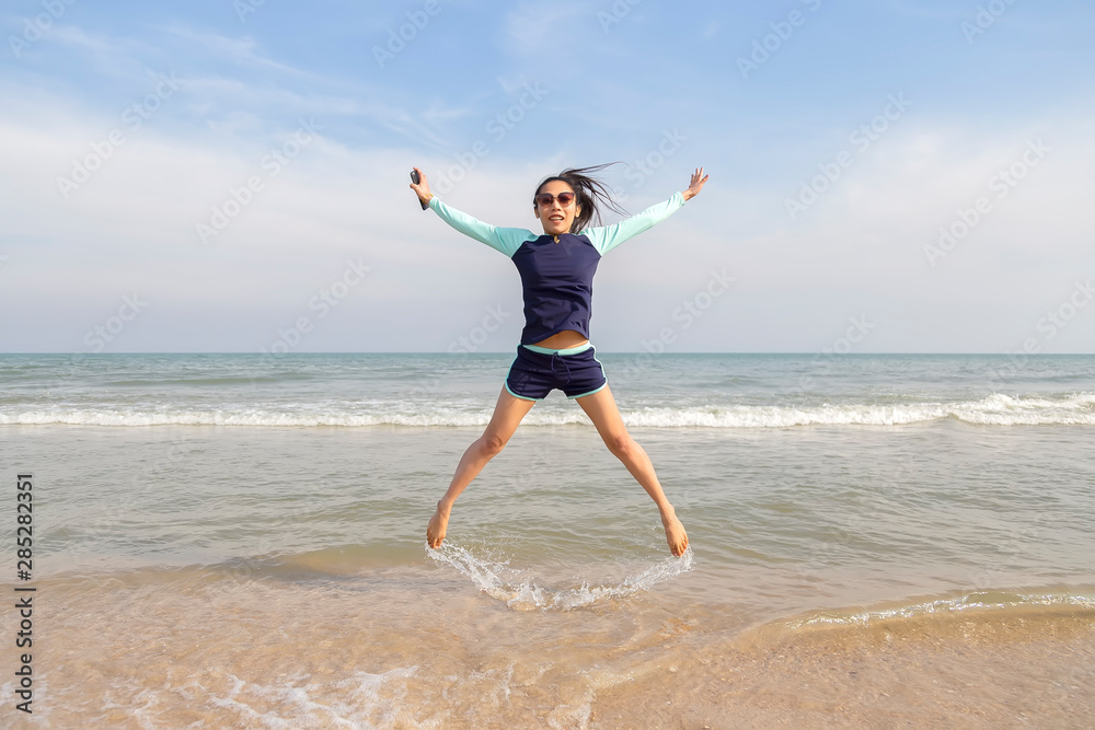 Asian women in bathing suits are jumping on the sand. Thai teenagers are playing at the beach during the daytime.